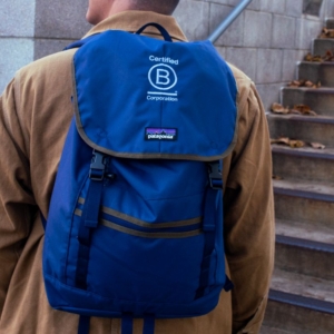 A man on a city sidewalk wearing a blue B Lab backpack
