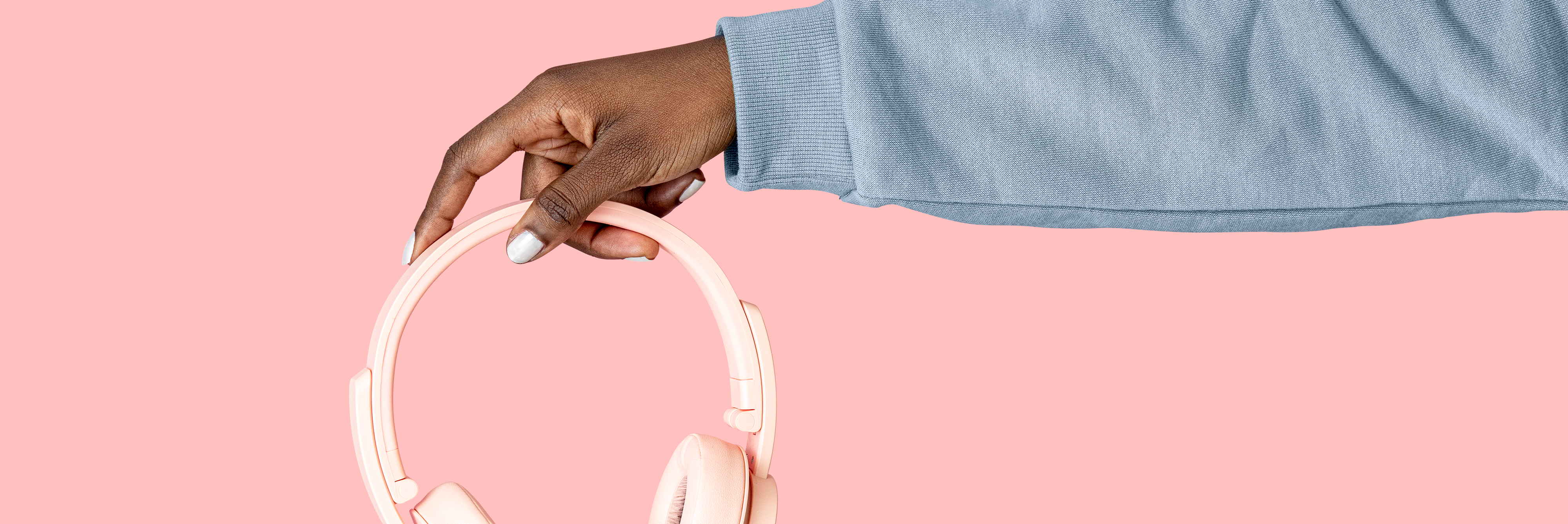 Hand holding headphones against pink backdrop