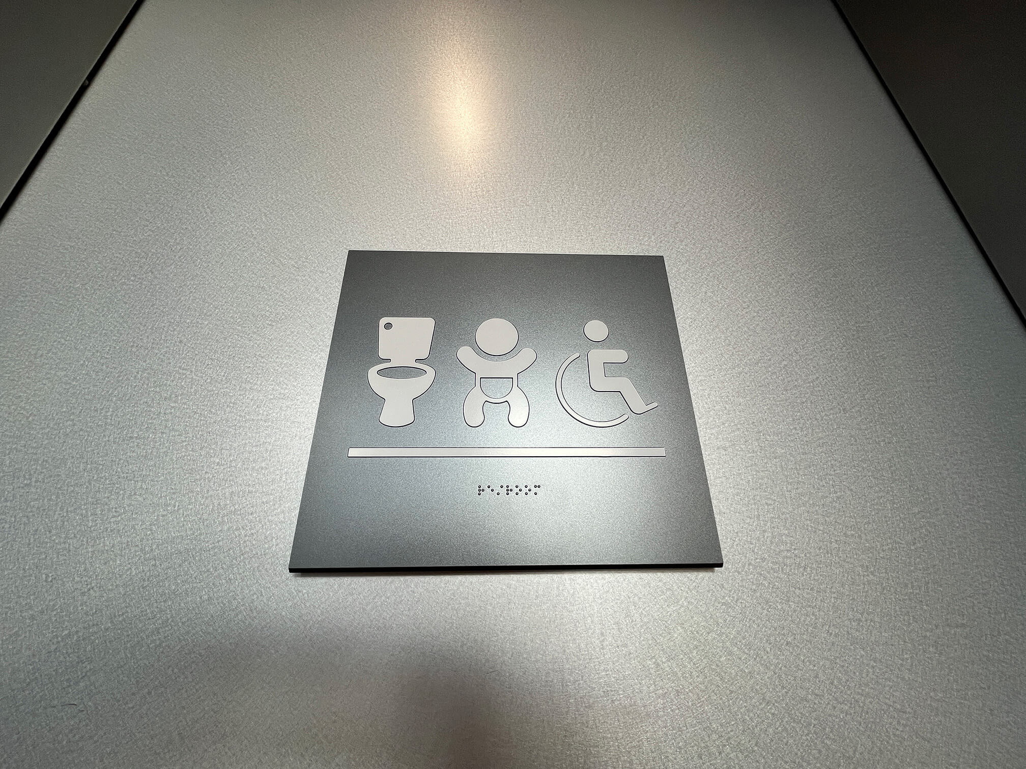 Typical signage for universal restrooms, with tactile symbols and braille facing the front, towards the approaching user.