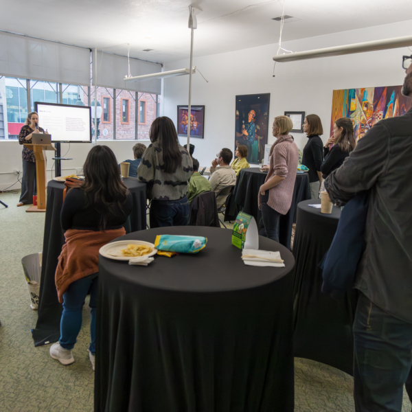 A woman speaks to a small crowd of B Corp leaders in a meeting room.