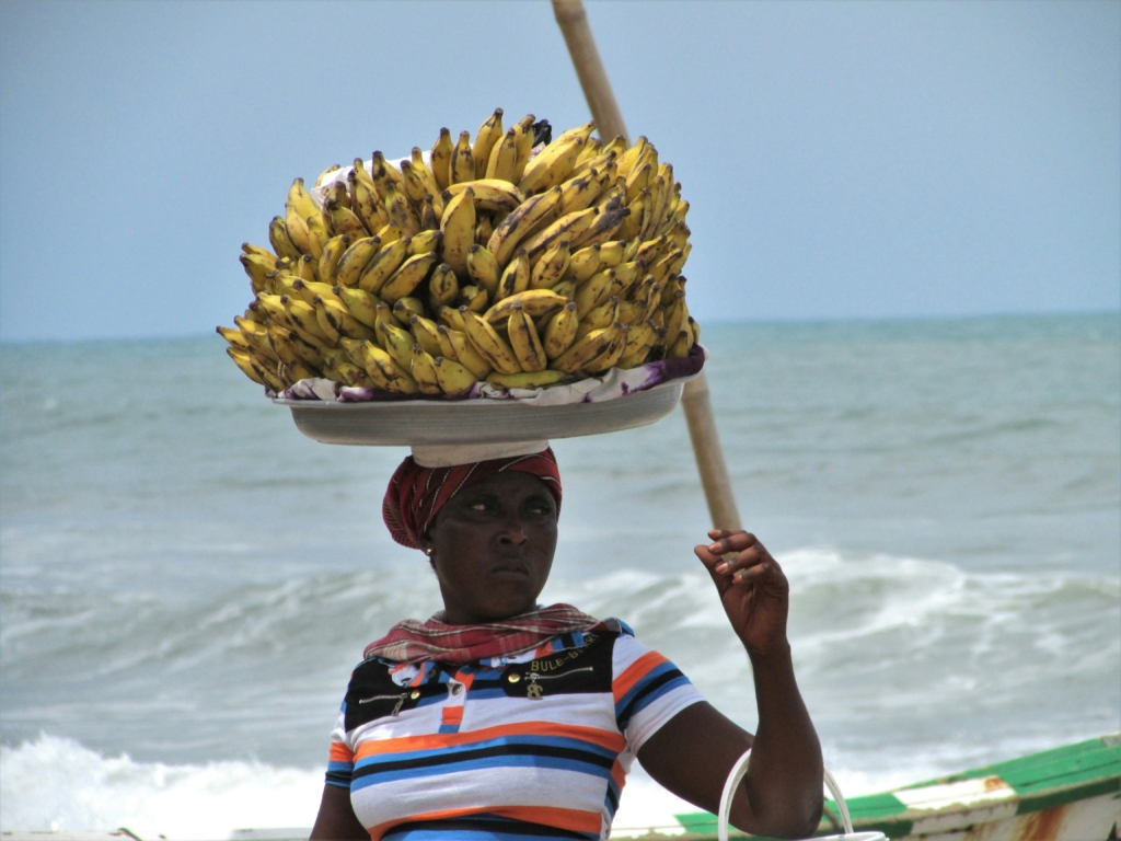 A female merchant in Ghana with a large tray of bananas balanced on her head 
